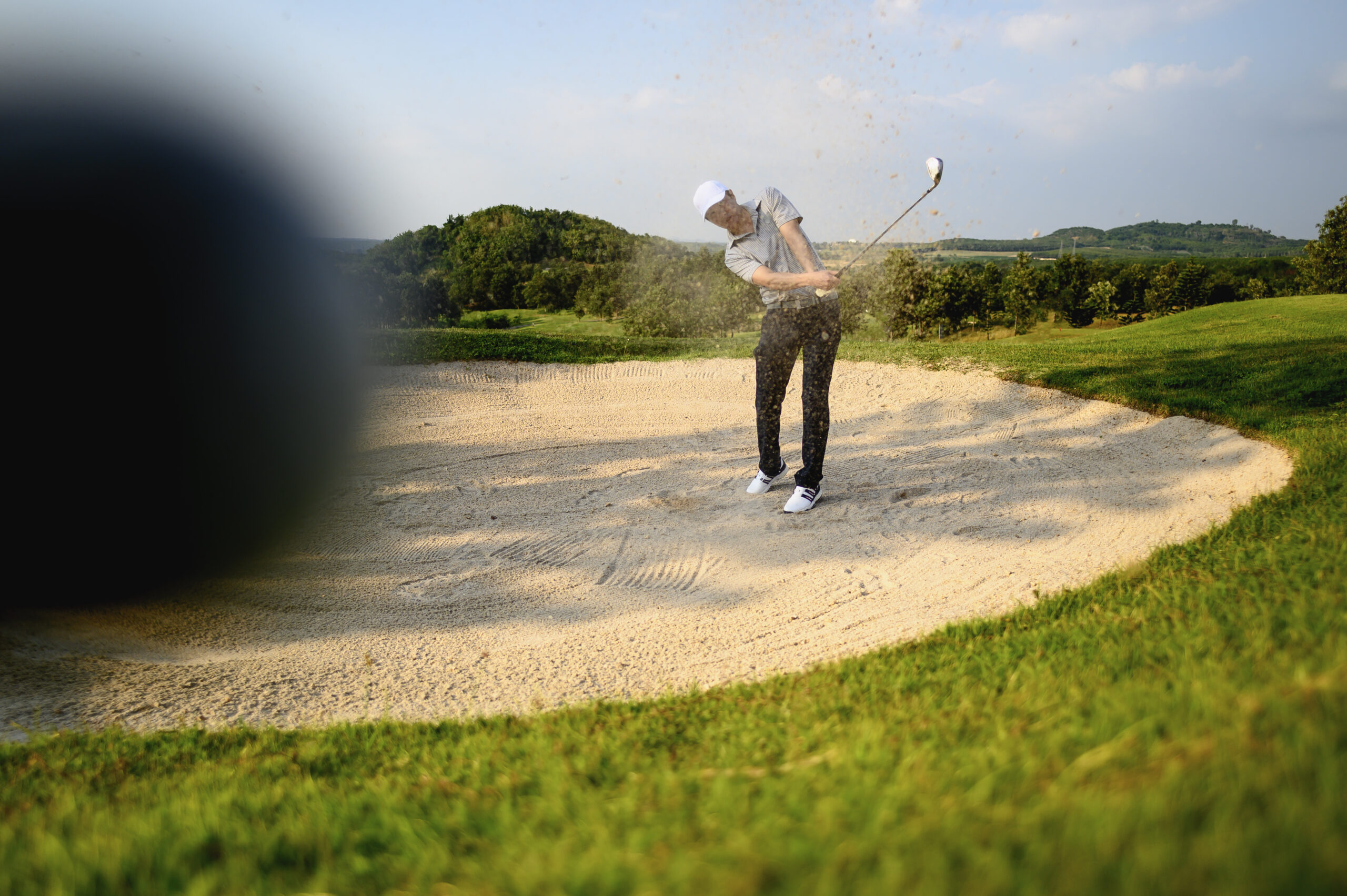 A golfer in action on a sunlit golf course, a close-up shot of a golf ball momentarily blurred as the golfer executes a precision swing